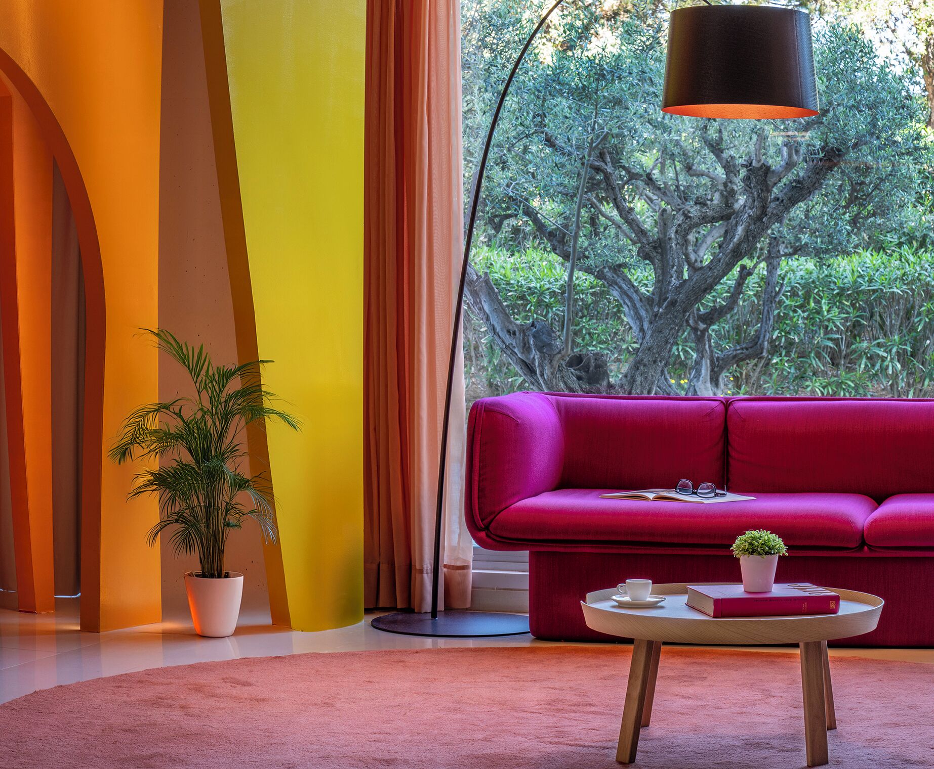 Una sala de estar moderna con un sofá rojo intenso, una mesa de centro redonda de madera y una planta en maceta.