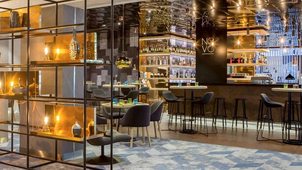 Eine moderne Bar mit Glastrennwand, Barhocker und einer Auswahl an Flaschen und Gläsern auf Regalen.