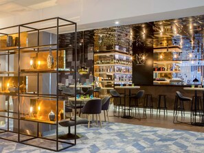 Un espace bar moderne, doté d’une cloison en verre, de tabourets de bar et de différentes bouteilles et verres exposés sur des étagères.