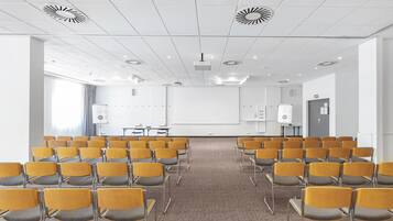 A conference room with rows of yellow chairs, a whiteboard, and a projector on the ceiling.