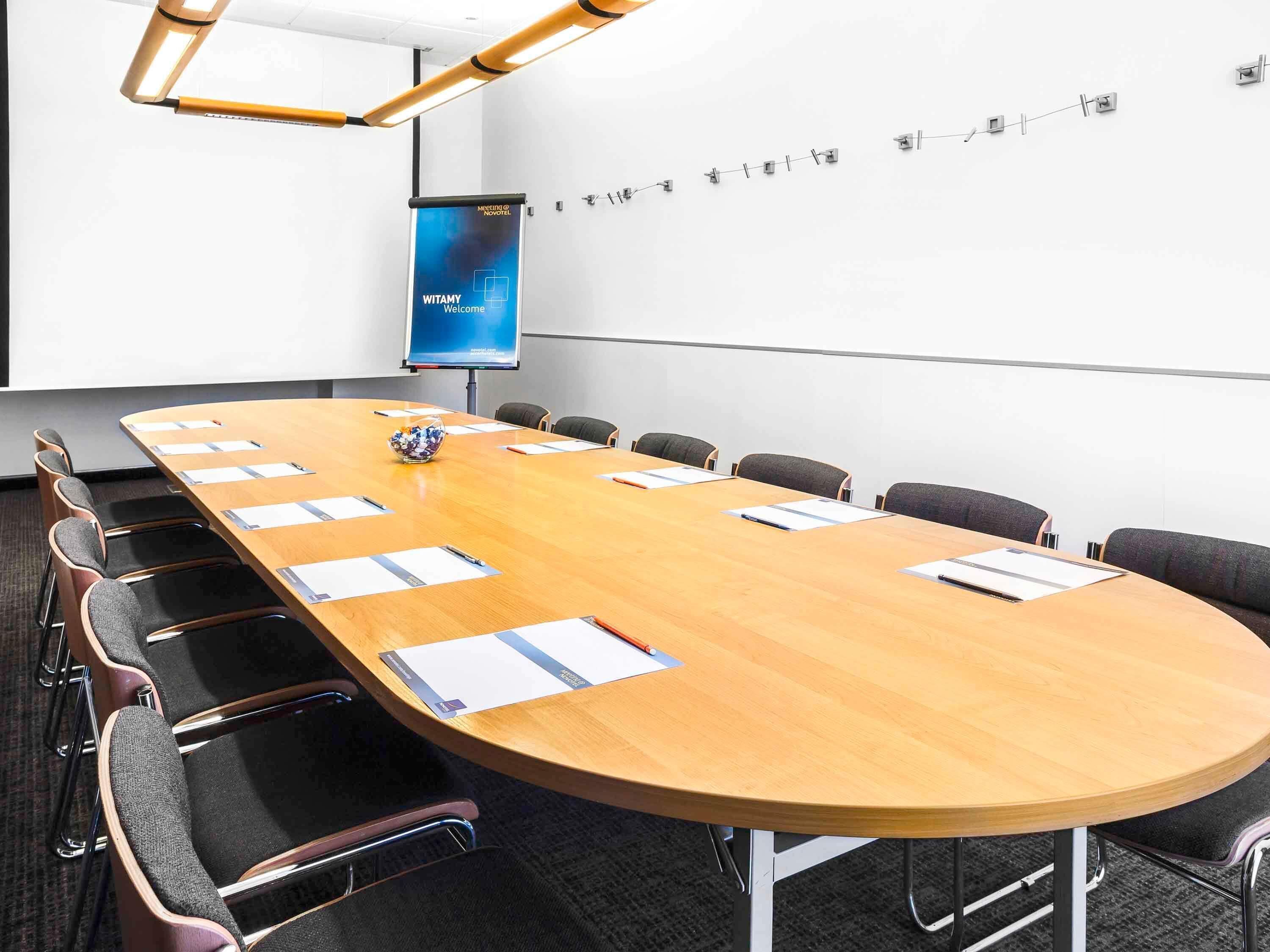 A conference room with a long table, chairs, a projector screen, and a whiteboard.