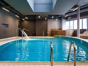 Una piscina interior con agua cristalina, una escalera de metal y una pared con un letrero que dice 'IN BALANCE BY HOUDEVILLE'.