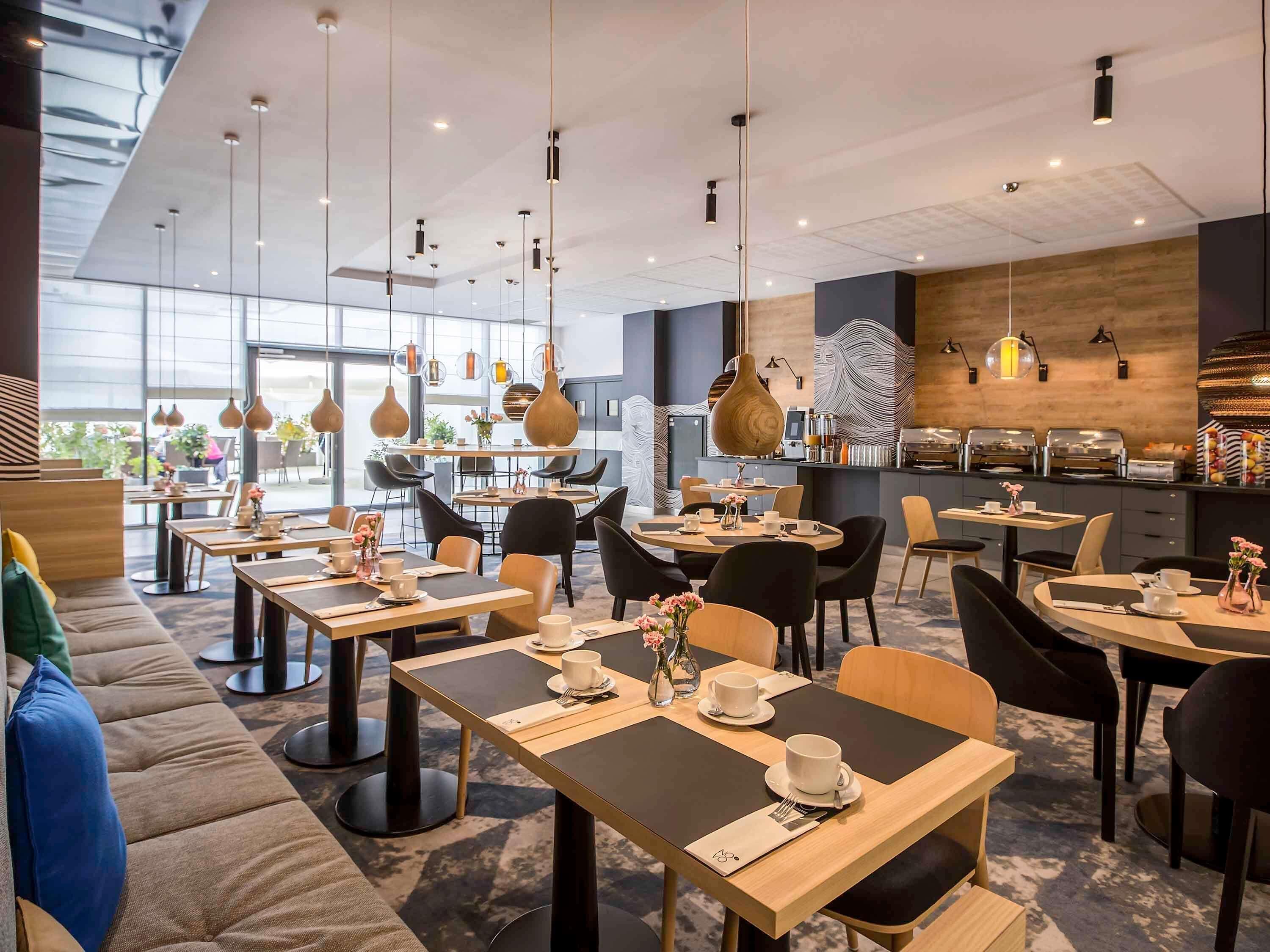 Una cafetería moderna con varias mesas y sillas, una barra de café y vistas al exterior.
