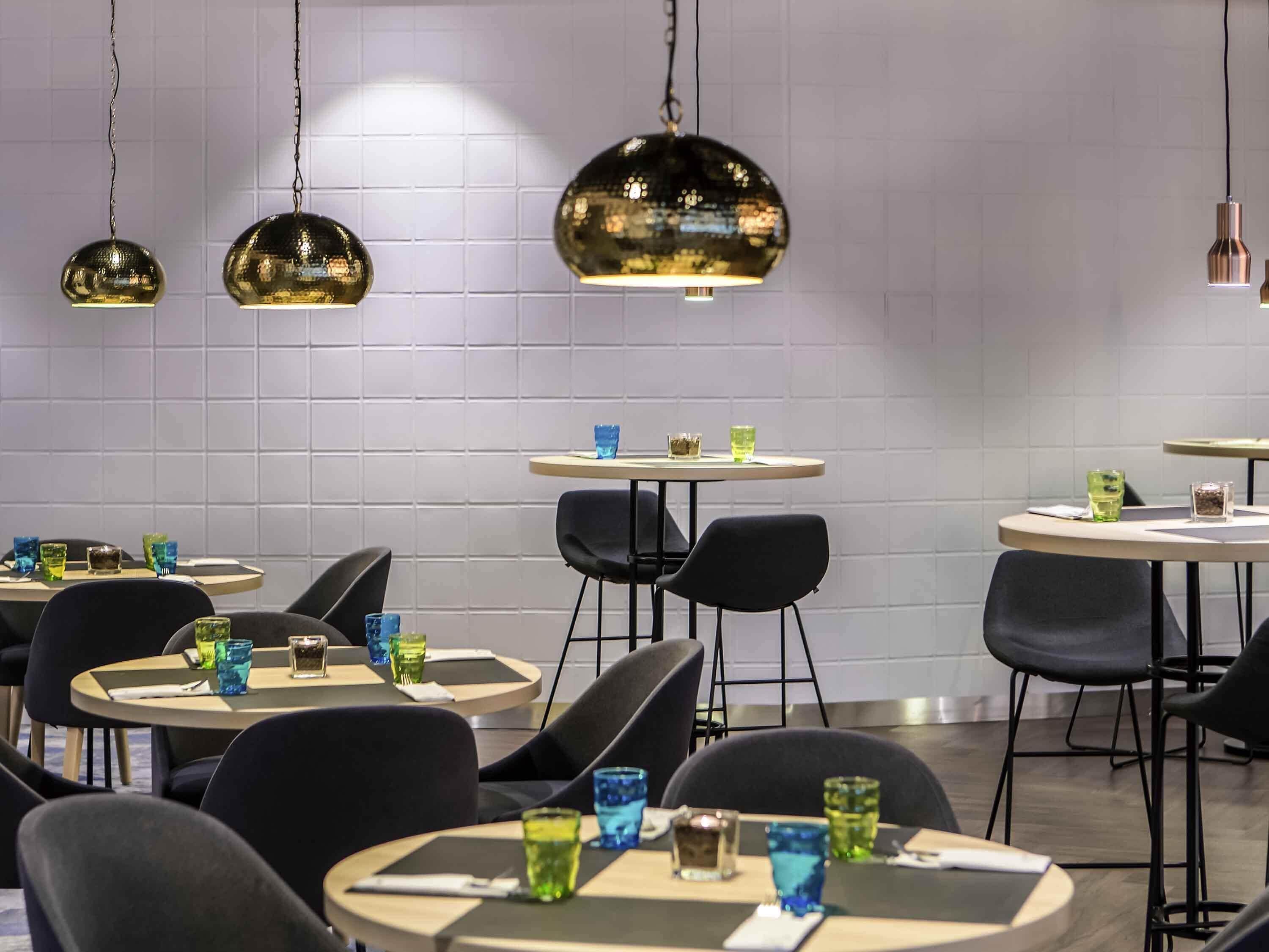 A modern dining area with round tables, black chairs, and pendant lighting.
