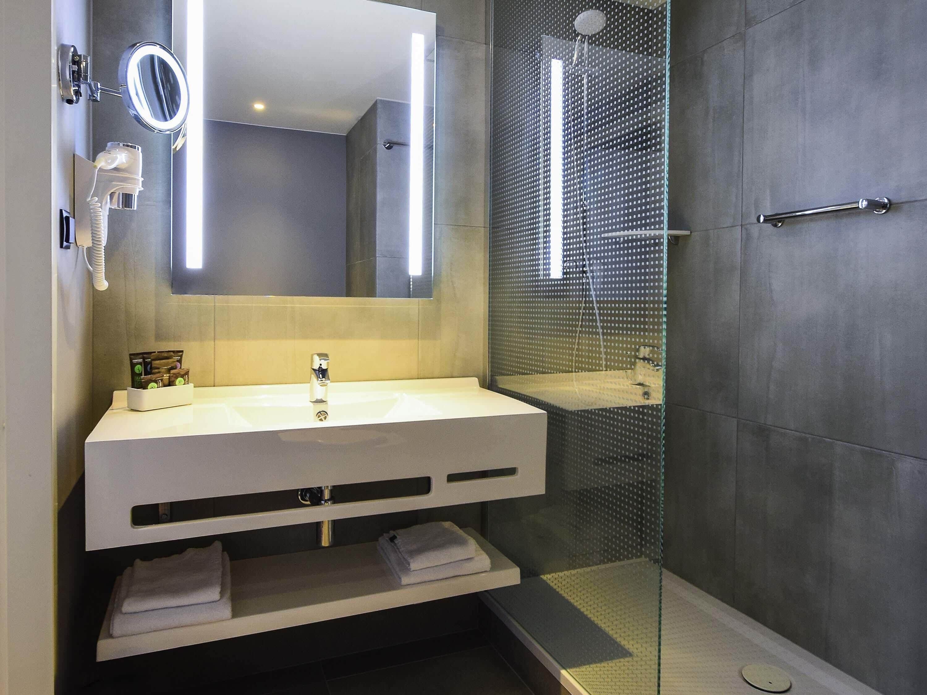 A modern bathroom with a white sink, a mirror, a handheld showerhead, and a glass-enclosed shower.