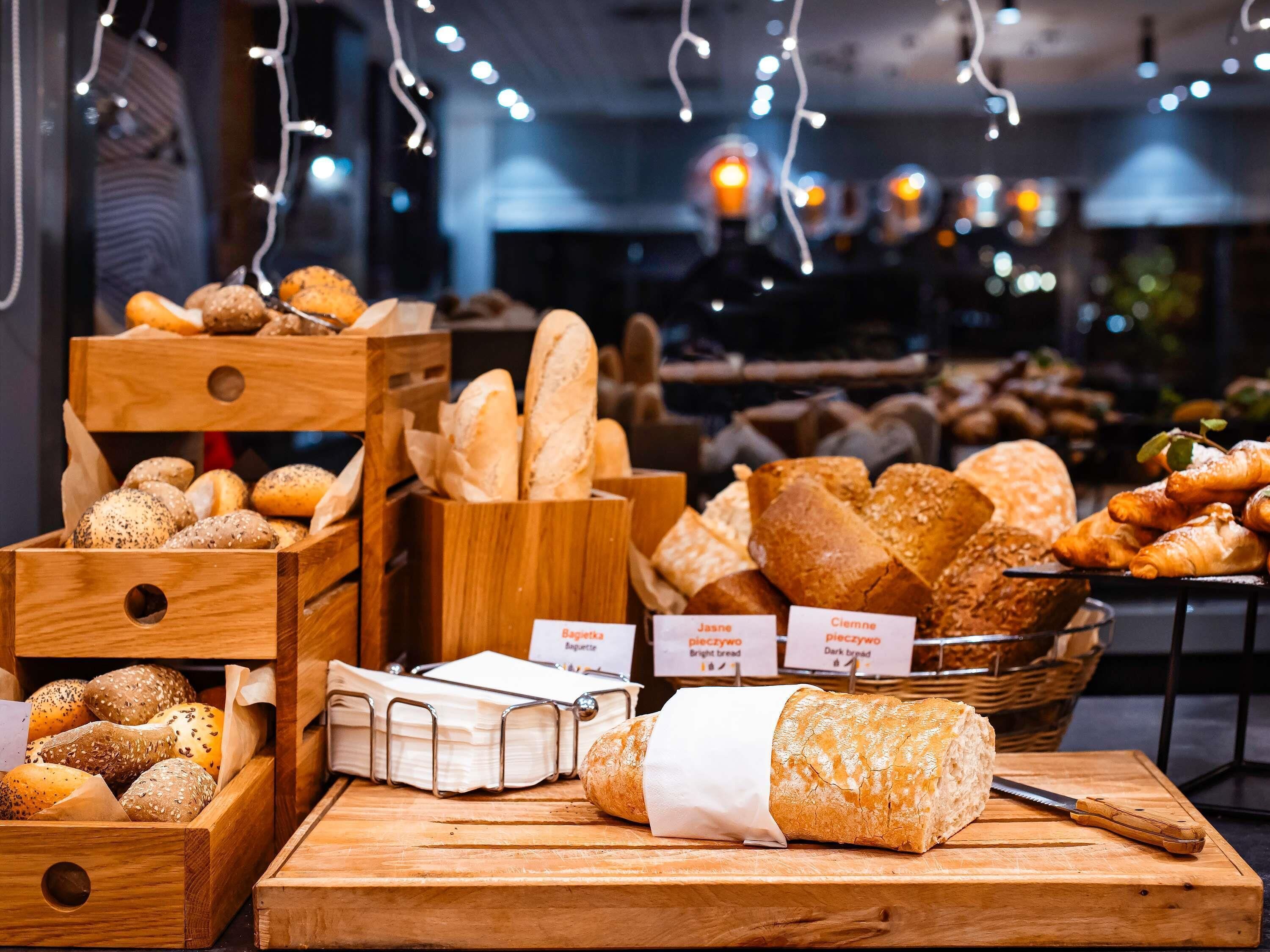 Variedad de panes y pasteles exhibidos en cajas y cestas de madera, con etiquetas que señalan tipos como 'Raspa' y 'Jasne'.