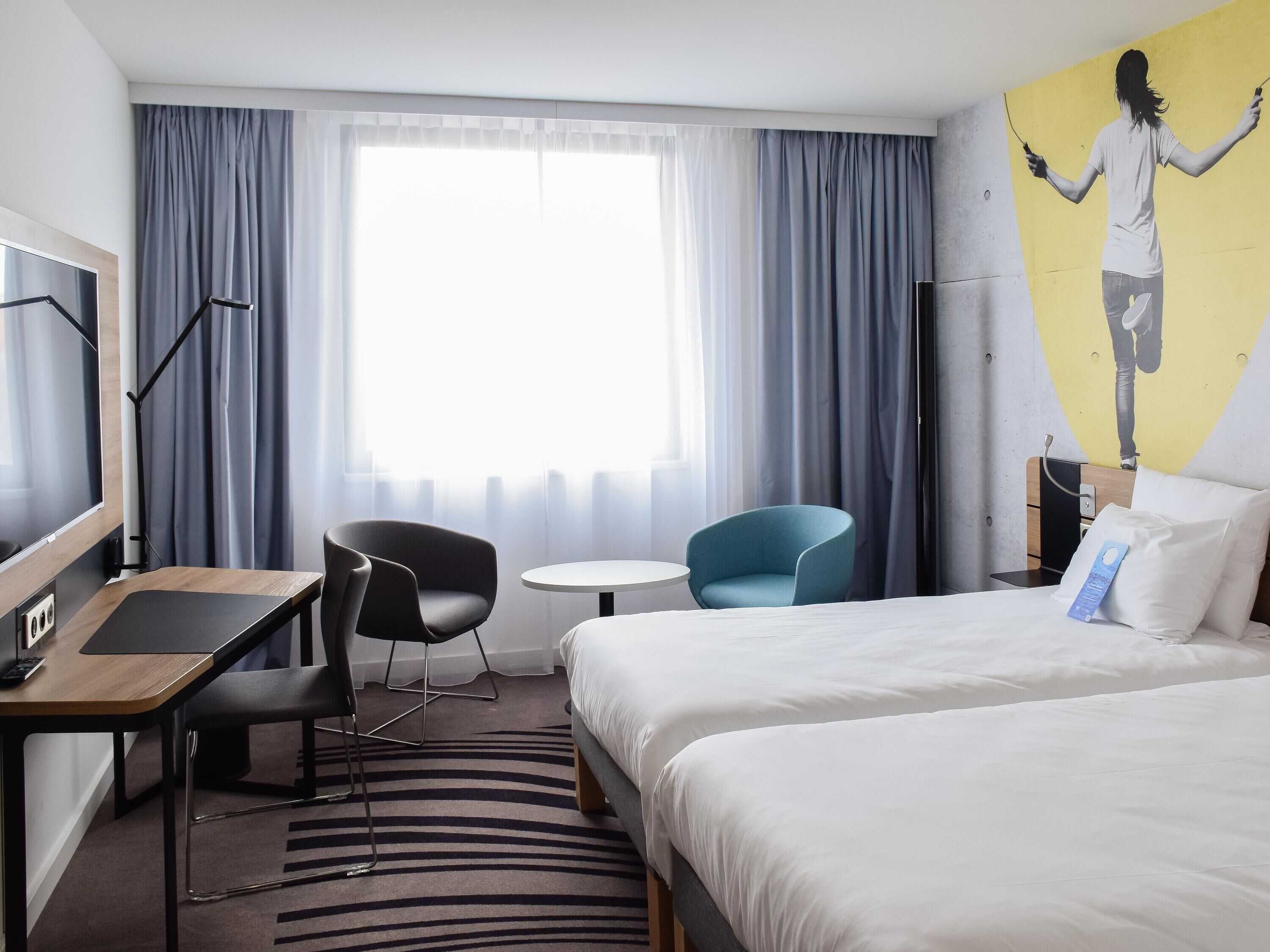Une chambre d’hôtel avec un lit, un bureau, une chaise, une petite table et un téléviseur.