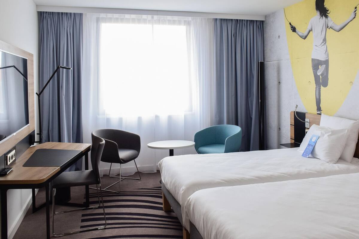 Hotellihuone, jossa on sänky, työpöytä, tuoli, pieni pöytä ja televisio.
