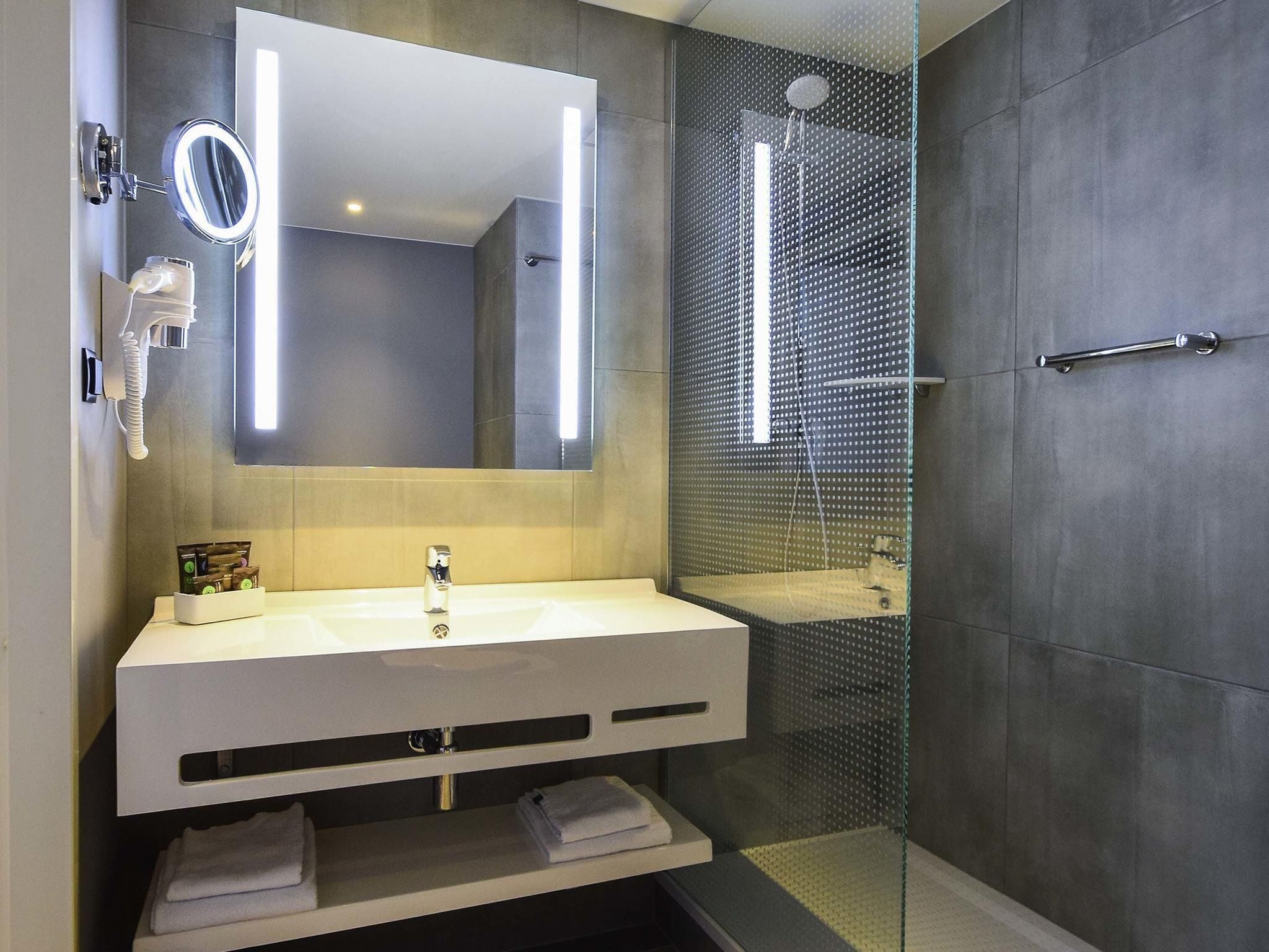 Un baño moderno con tocador blanco, un espejo grande, cabina de ducha de vidrio y un perchero para toallas.
