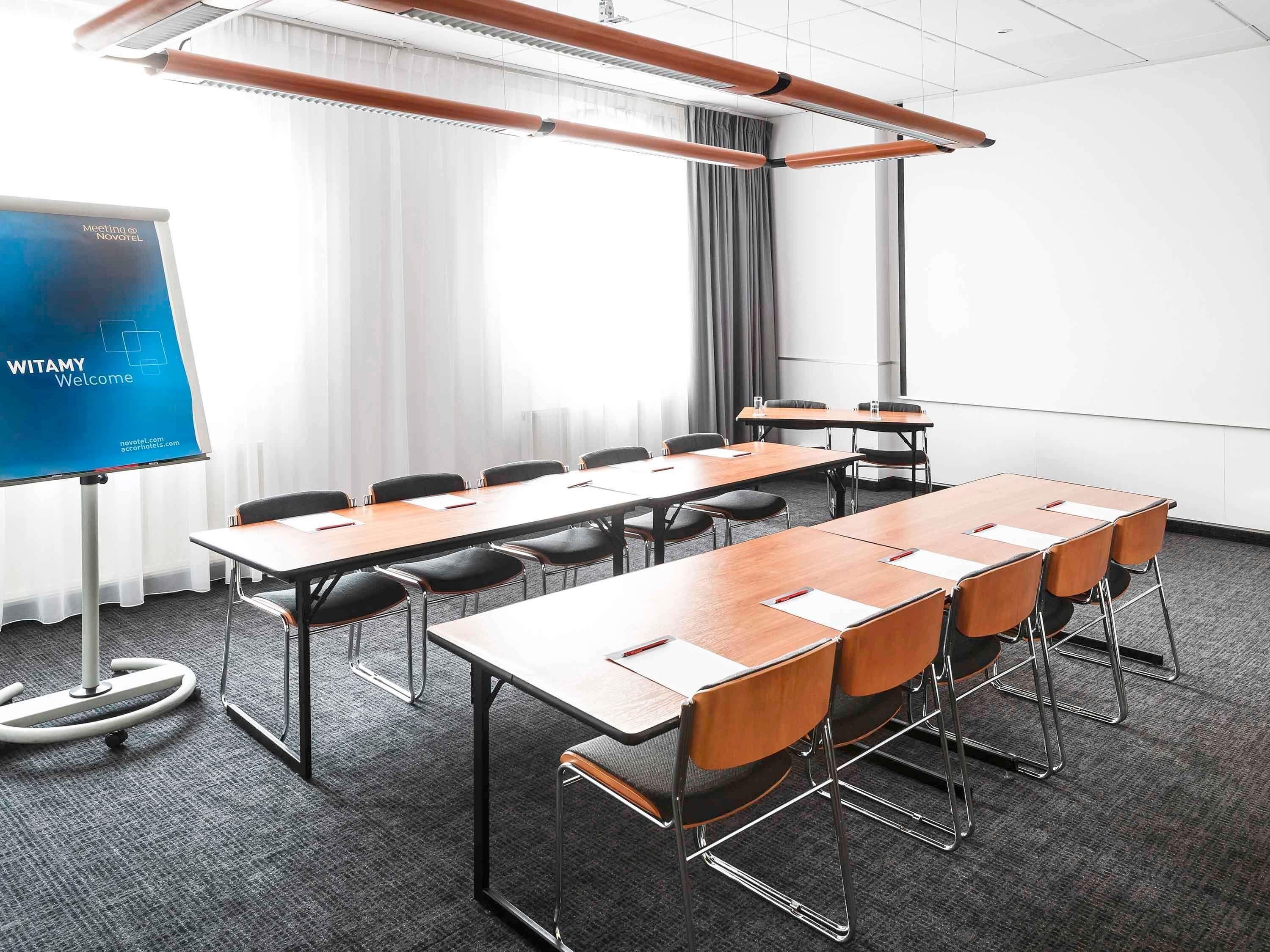 A meeting room with a long table, chairs, a projector screen, and a window with curtains.