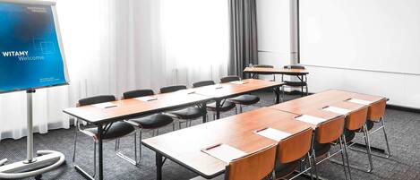 A meeting room with a long table, chairs, a projector screen, and a window with curtains.