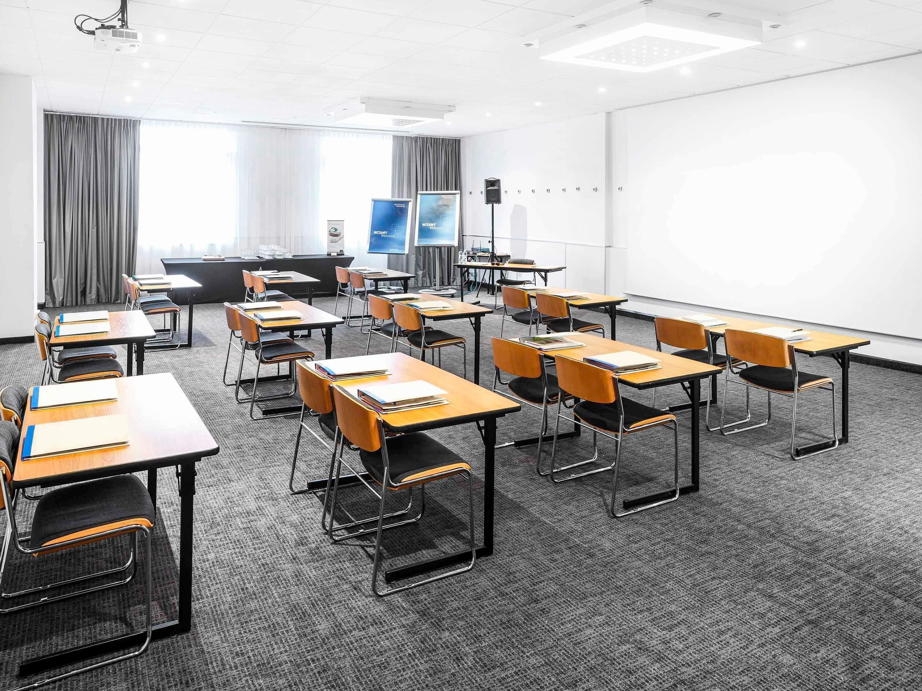 A conference room with multiple tables and chairs, a projector, and a large screen.