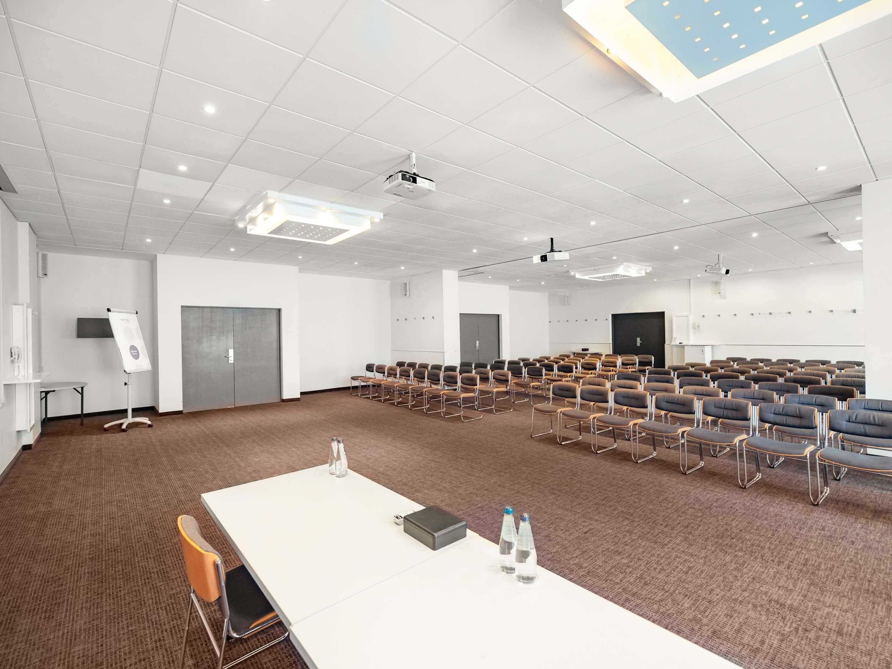 A conference room with rows of chairs, a whiteboard, a projector, and a table with water bottles.