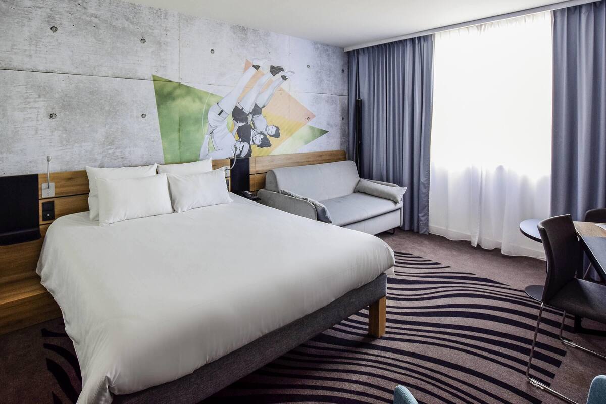Hotellihuone, jossa on sänky, sohva, pieni pöytä ja tuoli.