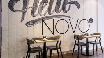 Ein modernes Café-Interieur mit einer großen Wandmalerei mit dem Schriftzug "Hello NOVO²" und zwei Tischen mit Stühlen.