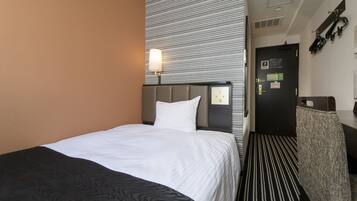 Habitación de hotel con cama, mesita de noche, lámpara de pared, puerta con lector de tarjeta y perchero.
