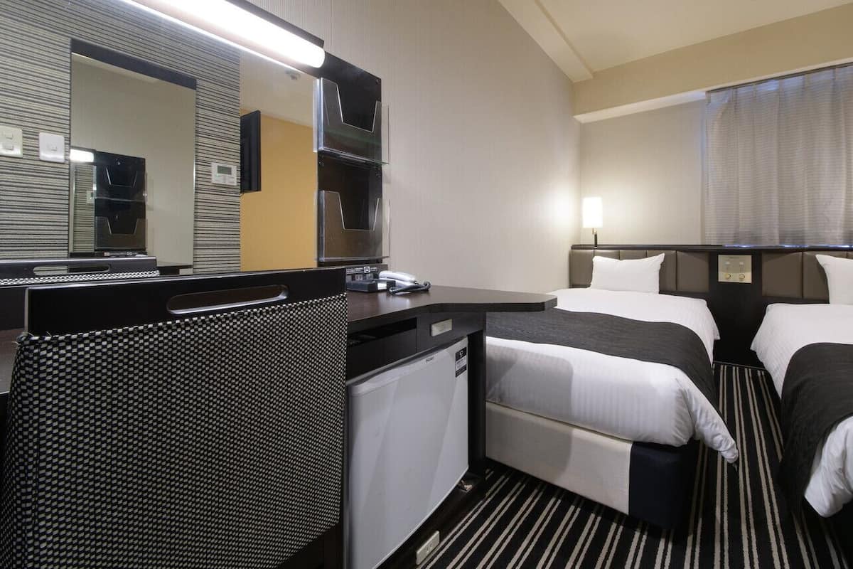Ein Hotelzimmer mit zwei Betten, einem Schreibtisch, einem kleinen Kühlschrank, einer Mikrowelle und einem großen Spiegel.