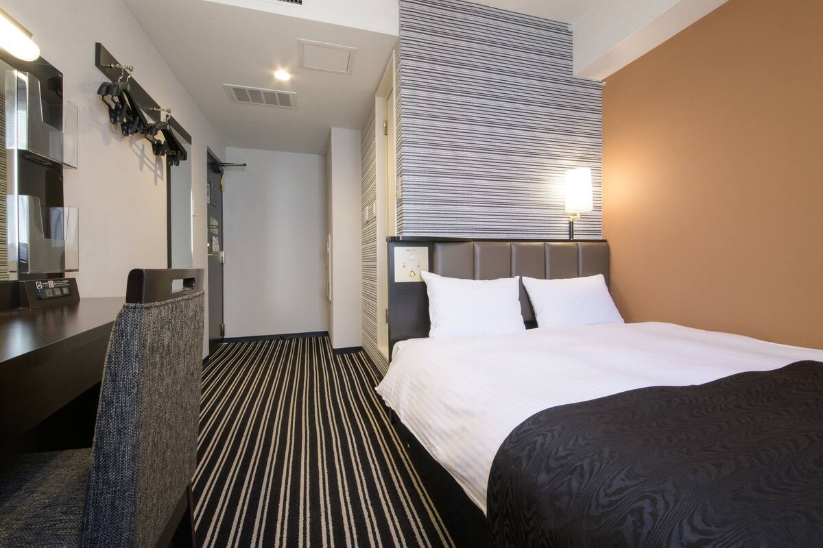 A hotel room with a bed, a desk, and a mirror.