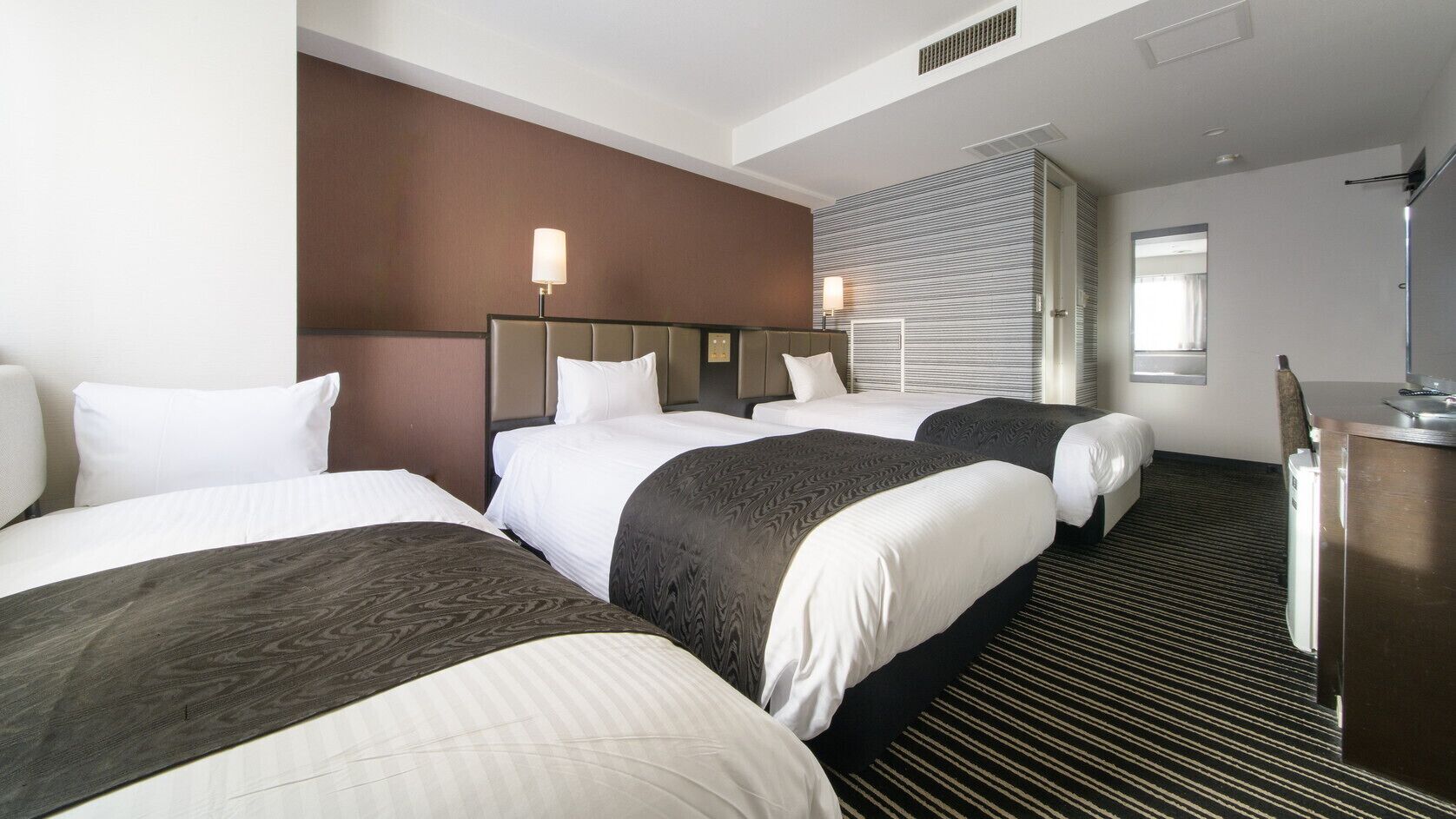 A hotel room with three beds, a desk, and a large window.