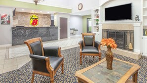 Un hall d’entrée comprenant deux fauteuils en cuir, une table basse, un vase avec des fleurs, un comptoir d’accueil, une cheminée et un téléviseur.