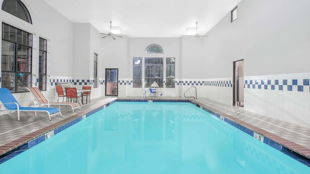 Une piscine entourée de chaises longues et dotée d’un parasol, le tout bordé de murs blancs et d’une bordure carrelée.