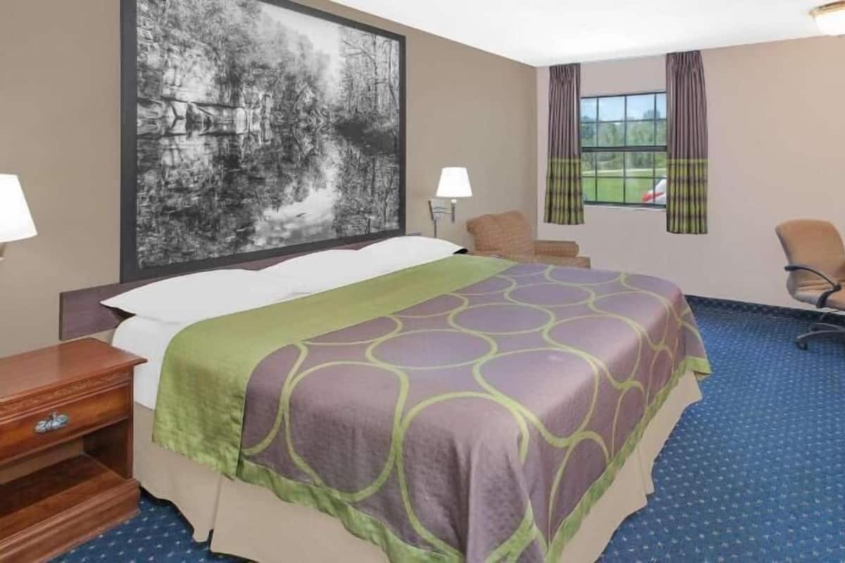 Ein Hotelzimmer mit einem Bett, einem Schreibtisch, einem Stuhl, einem Fernseher und einem Fenster mit Vorhängen.