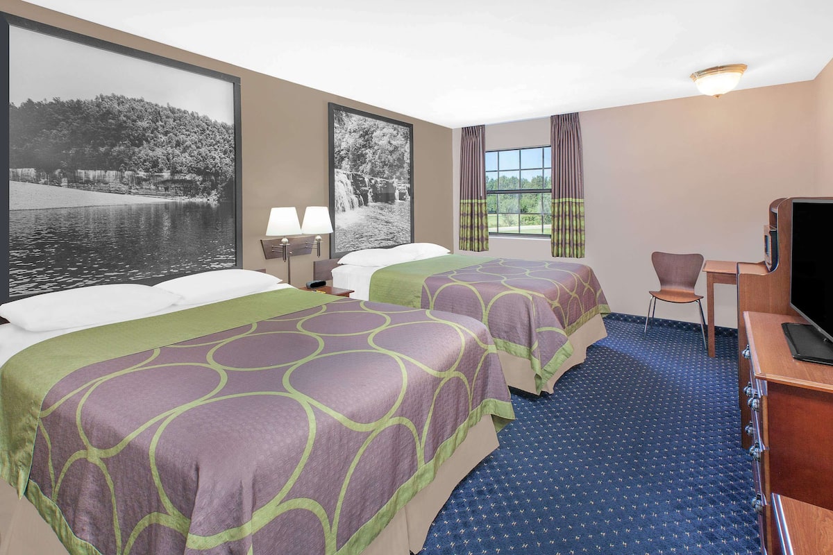 Ein Hotelzimmer mit zwei Betten, einem Schreibtisch mit Fernseher, einem Sessel und großen Fenstern mit Seeblick.