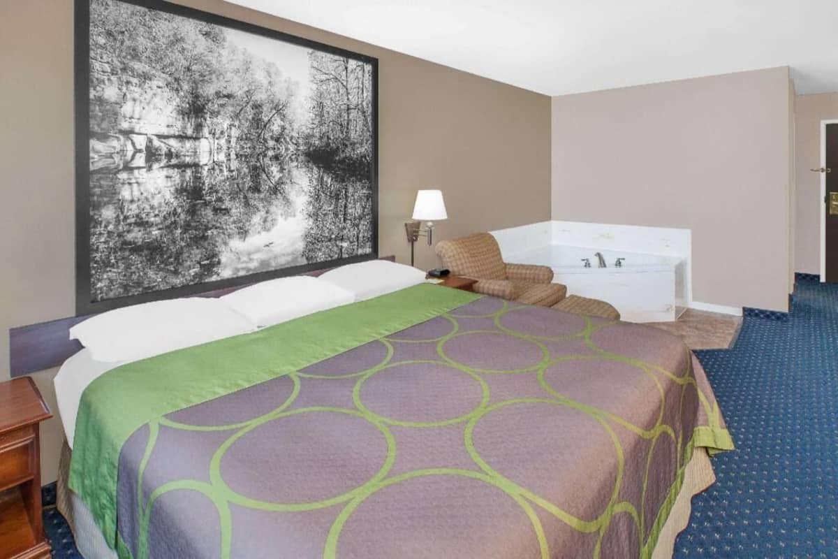 Ein Hotelzimmer mit einem großen Bett, einer Badewanne, einem Wandbild und einer Lampe.
