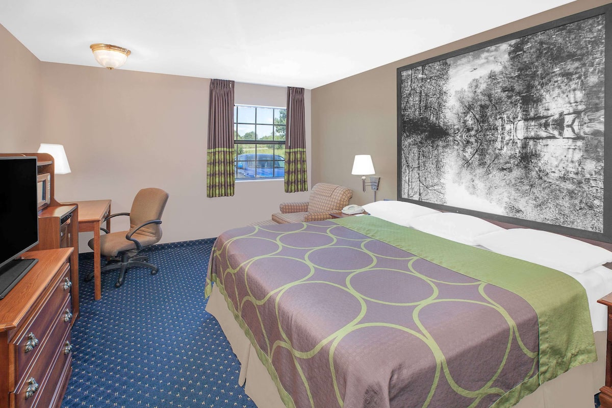 Ein Hotelzimmer mit Bett, Schreibtisch, Stuhl, Fernseher und einem großen Gemälde an der Wand.