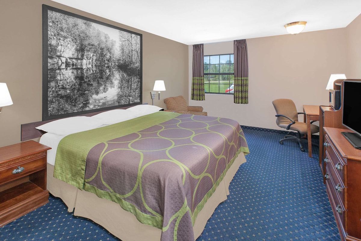 Ein Hotelzimmer mit einem großen Bett, einem Schreibtisch mit Computer, einem Sessel und einem Fernseher.