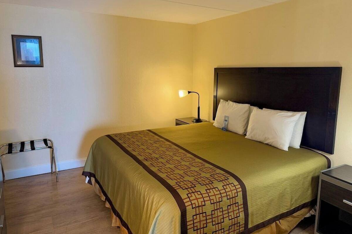 A hotel room with a bed, bedside tables, a nightstand, a chair, and a wall-mounted lamp.