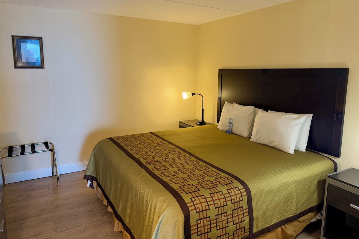 A hotel room with a bed, a nightstand, a lamp, a chair, and a picture on the wall.