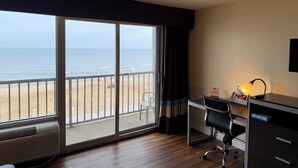 Et hotelværelse med en stor skydedør til stranden, et skrivebord med stol, en lampe og et lille bord med et skilt.
