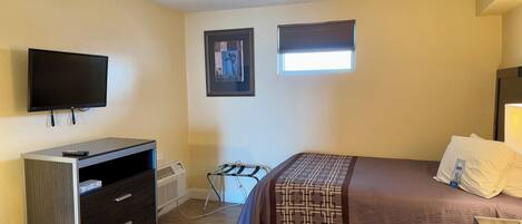 A hotel room with two beds, a TV, a dresser, and a window with blinds.
