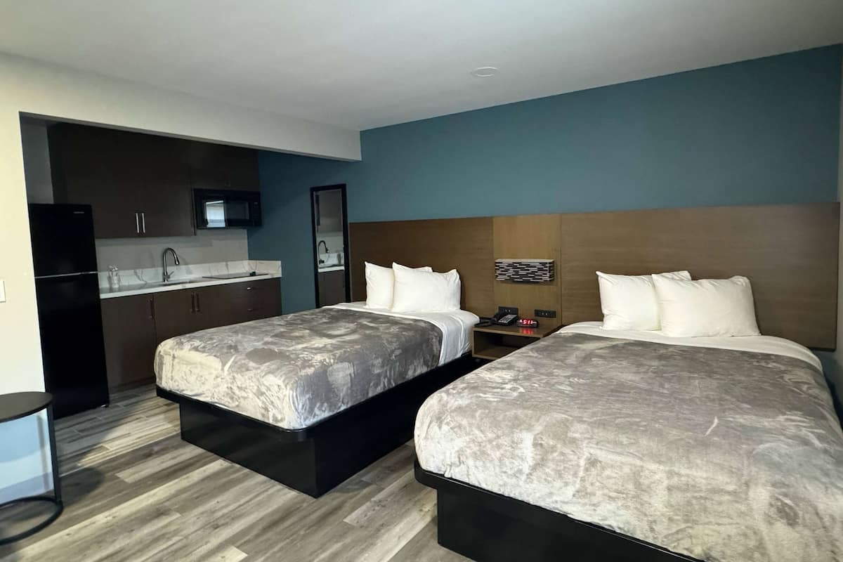 A hotel room with two beds, a kitchenette, and a bathroom.