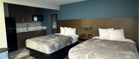 A hotel room with two beds, a kitchenette, and a bathroom.