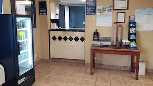 A hotel reception area with a refrigerator stocked with beverages, a coffee machine, and a table with coffee cups and a menu. - Baymont by Wyndham Coalinga (Coalinga)