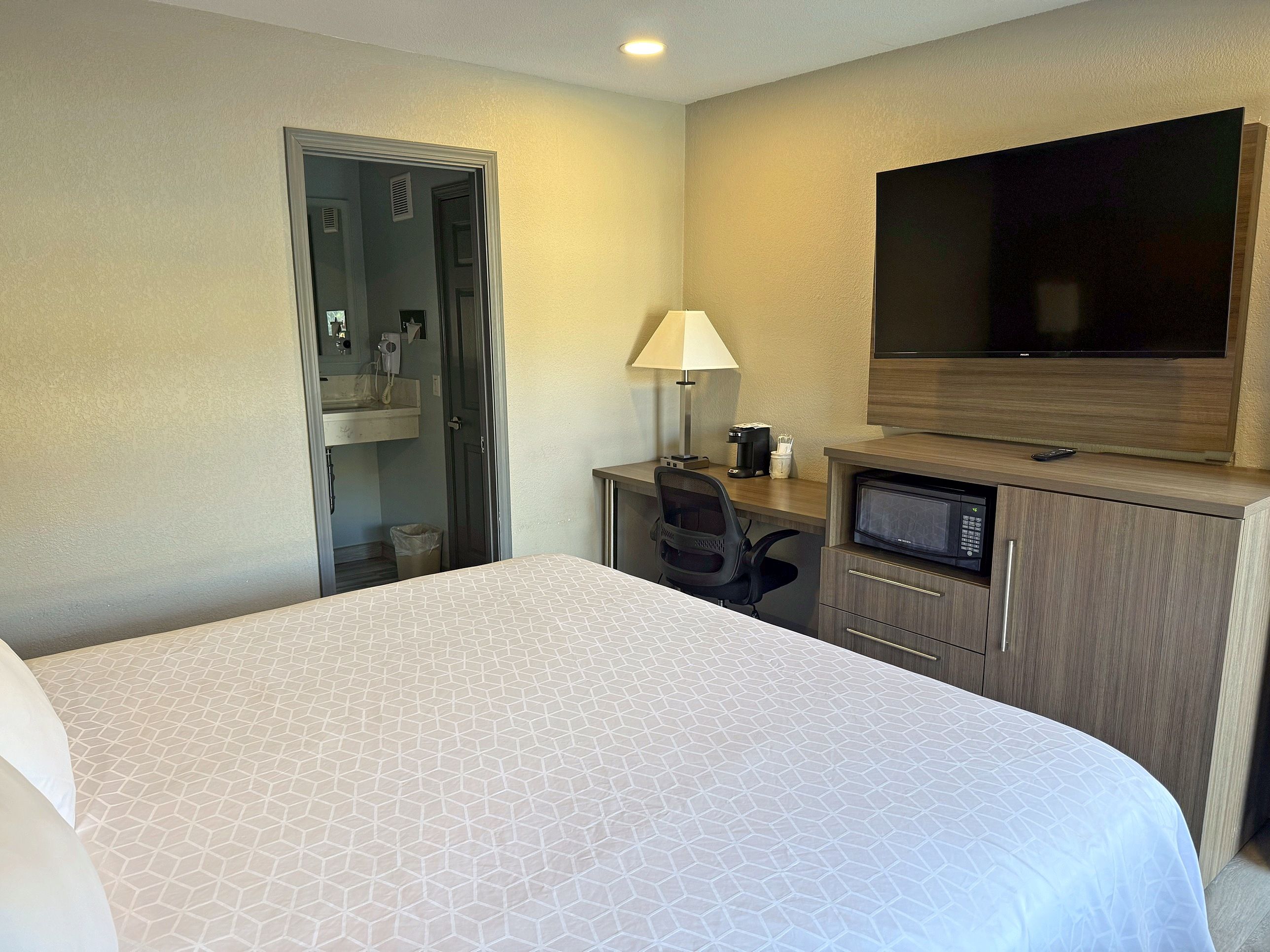 A hotel room with a large bed, a desk with a computer, a TV, and a bathroom.