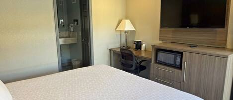 A hotel room with a large bed, a desk with a computer, a TV, and a bathroom.