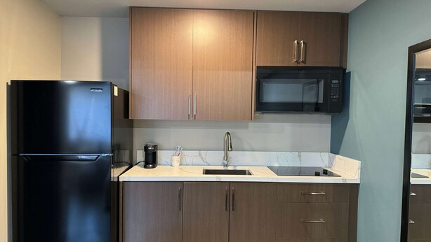 A modern kitchen with dark wooden cabinets, a black refrigerator, a microwave, and a sink. - Baymont by Wyndham Coalinga (Coalinga)