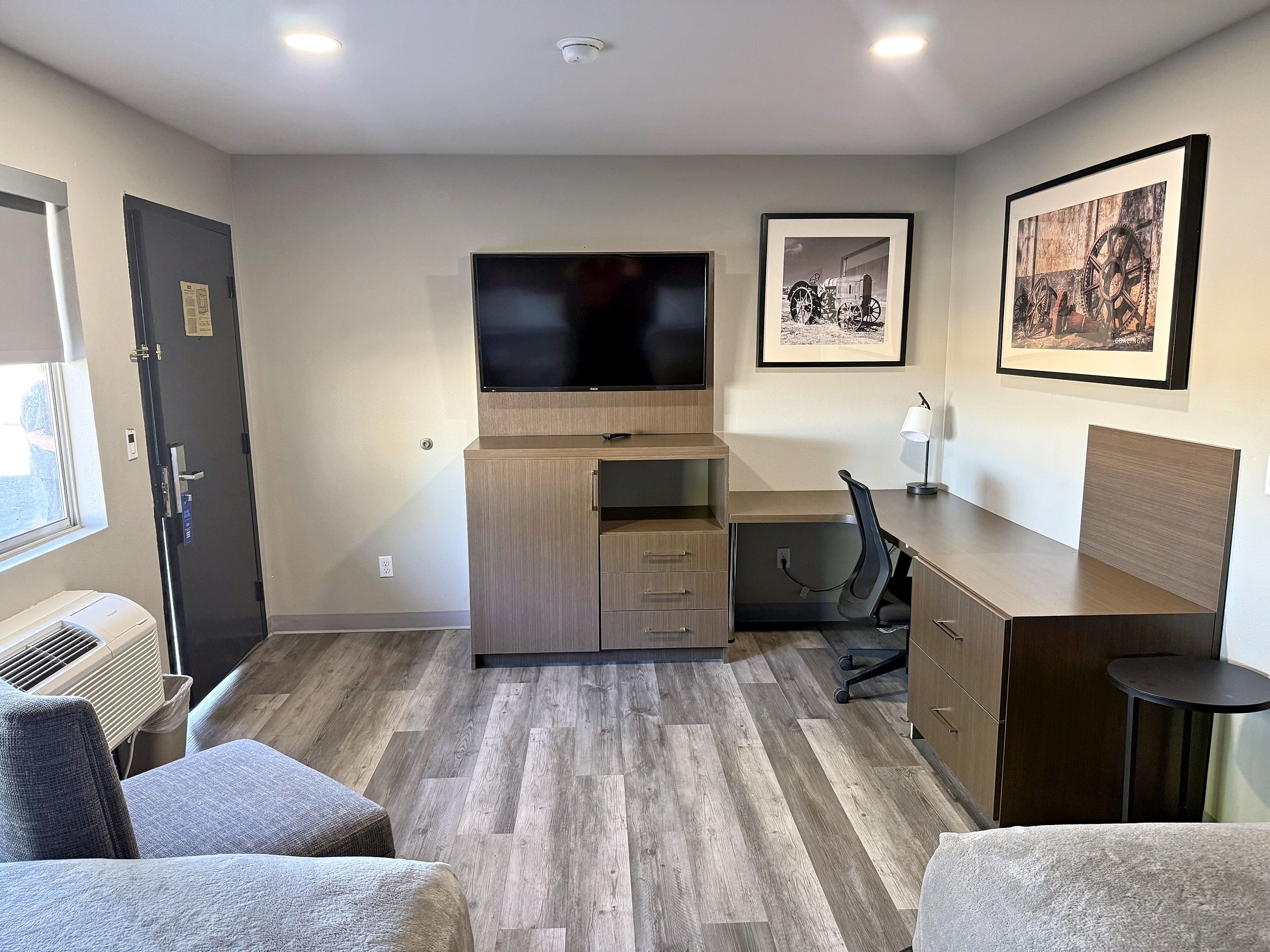 A compact hotel room with a flat-screen TV, a desk, a chair, and a bed.