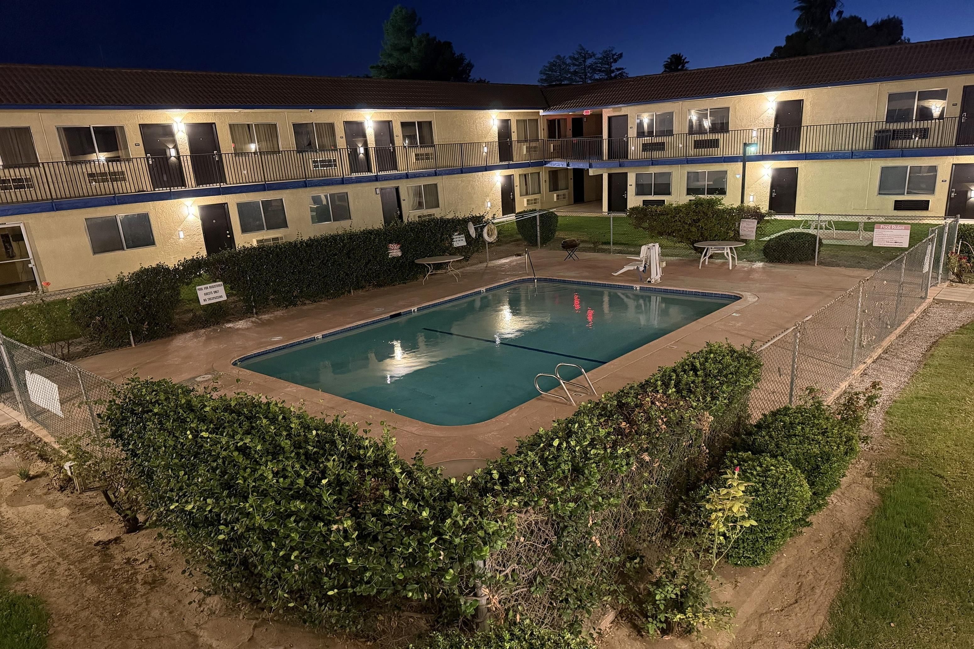 A hotel with a swimming pool surrounded by greenery and a fenced area.