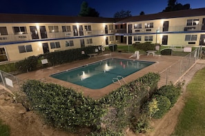 A hotel with a swimming pool surrounded by greenery and a fenced area.