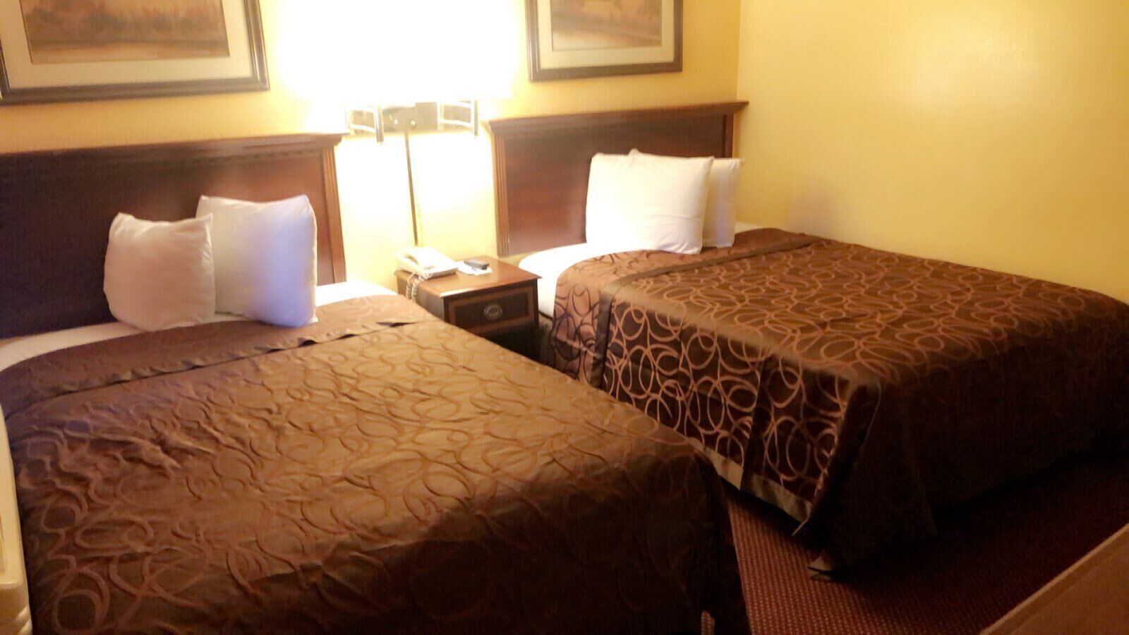 Habitación de hotel con dos camas, cada una con una colcha estampada, una mesita de noche con lámpara y teléfono.