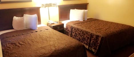Habitación de hotel con dos camas, cada una con una colcha estampada, una mesita de noche con lámpara y teléfono.
