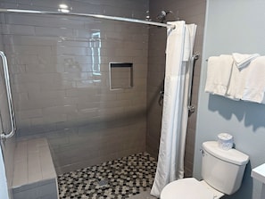A shower area with a glass door, a white shower curtain, and a toilet with a toilet paper roll. - Baymont by Wyndham Coalinga (Coalinga)
