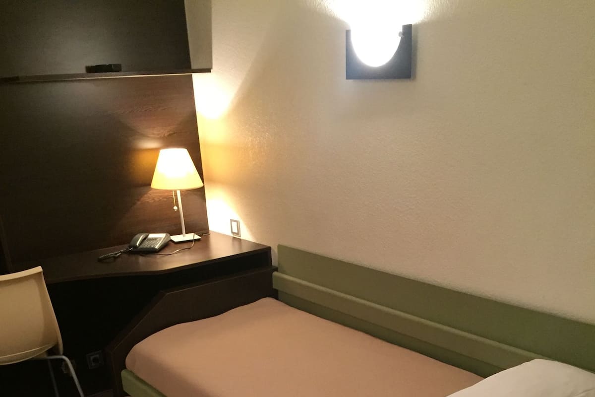 A twin bed with a green headboard and white bedding, a bedside table with a lamp, and a phone.