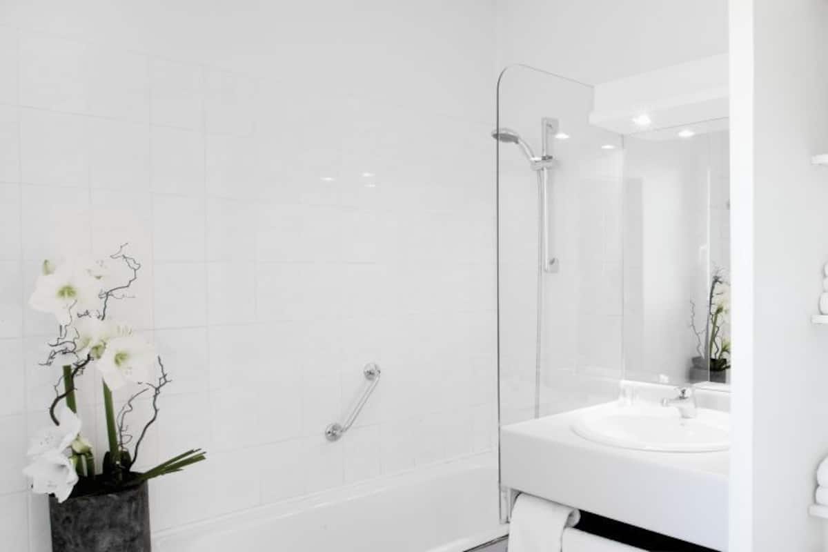 A modern bathroom with a glass shower enclosure, a white sink, and shelves with toiletries.
