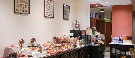 A buffet setup with various food items and beverages, a coffee machine, and a refrigerator.