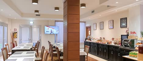 Un comedor con mesas y sillas, una encimera de cocina con alimentos y una pantalla de televisión.